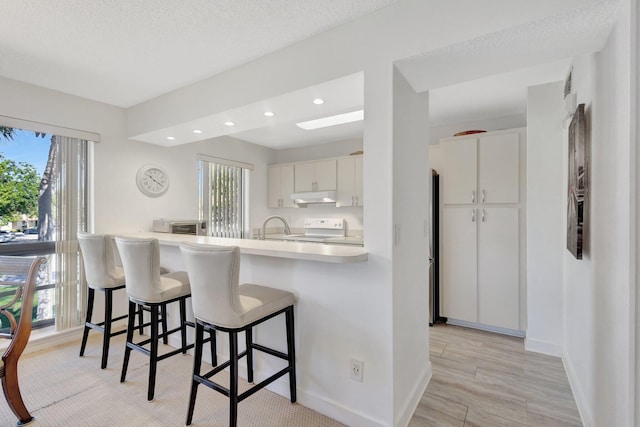 168 Brackenwood Rd, Palm Beach Gardens, FL 33418 - kitchen with under cabinet range hood, light countertops, a kitchen bar, electric range, and white cabinetry