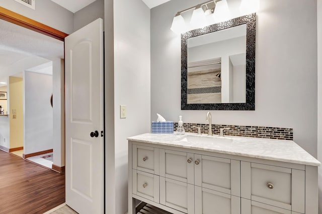 bathroom with visible vents, backsplash, wood finished floors, baseboards, and vanity