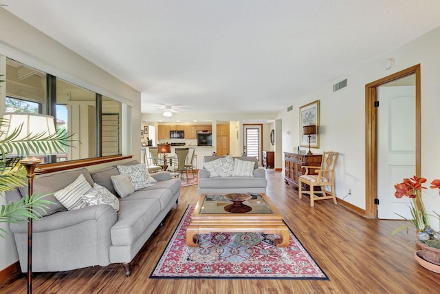 living room featuring a ceiling fan, wood finished floors, visible vents, and baseboards