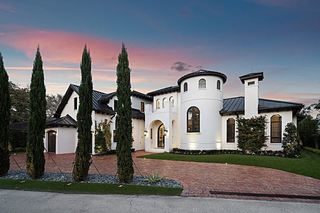 view of front facade with stucco siding, a standing seam roof, decorative driveway, a front yard, and metal roof