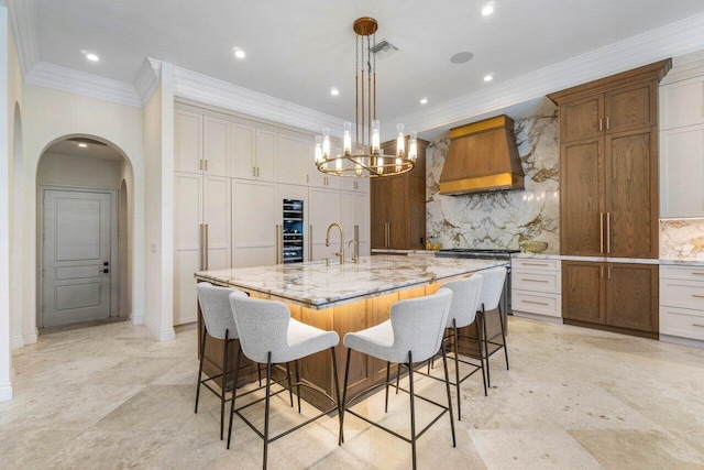 kitchen with tasteful backsplash, a spacious island, light stone countertops, premium range hood, and a kitchen bar