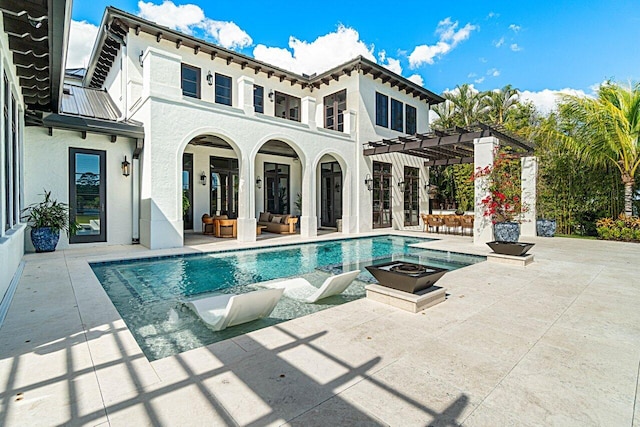 rear view of house with stucco siding, an outdoor living space with a fire pit, a pergola, and a patio area