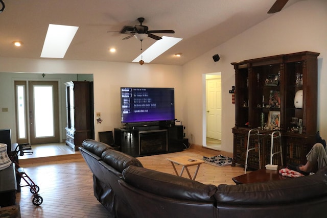 living room featuring lofted ceiling with skylight, a ceiling fan, and hardwood / wood-style flooring