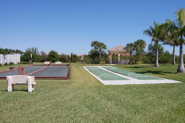 view of home's community with fence, shuffleboard, and a yard