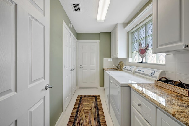 laundry room featuring visible vents, washing machine and clothes dryer, cabinet space, and light tile patterned floors