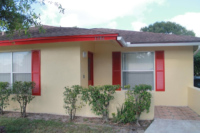 entrance to property with stucco siding and roof with shingles