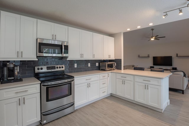 kitchen featuring a peninsula, light countertops, open floor plan, and appliances with stainless steel finishes