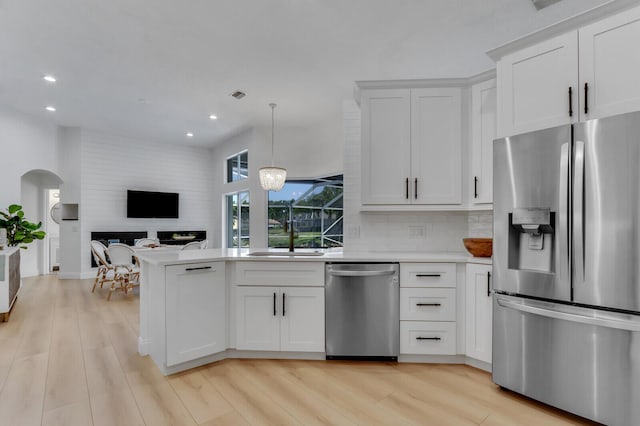 kitchen featuring a peninsula, stainless steel appliances, light countertops, open floor plan, and light wood-type flooring