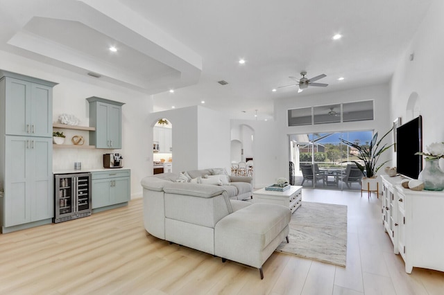 living area with a ceiling fan, a tray ceiling, recessed lighting, wine cooler, and arched walkways