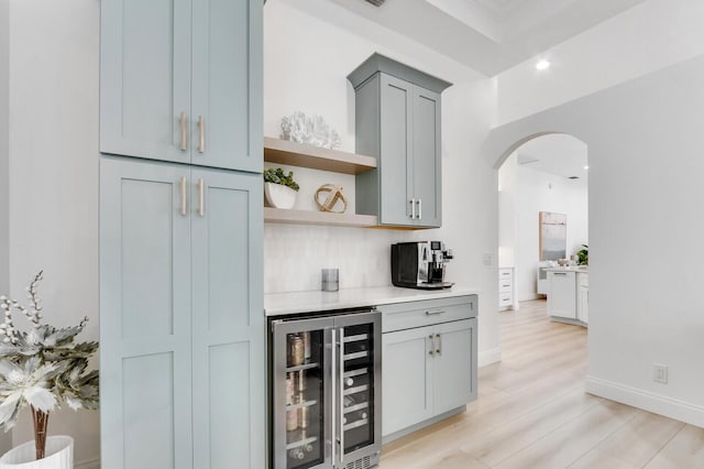 bar with light wood finished floors, backsplash, baseboards, wine cooler, and arched walkways