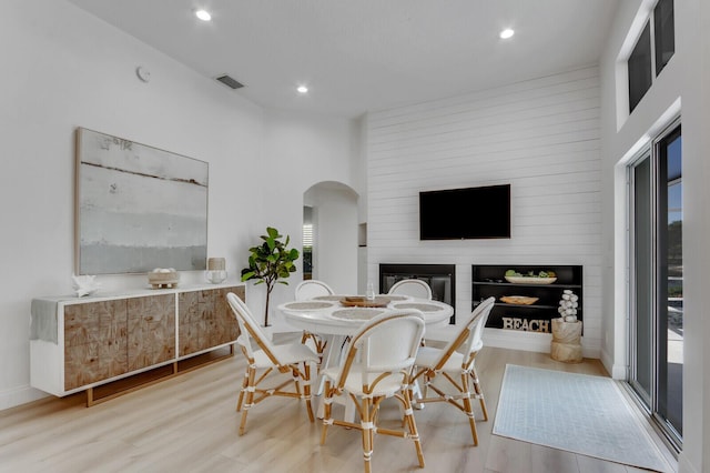 dining area featuring wood finished floors, visible vents, recessed lighting, arched walkways, and a glass covered fireplace