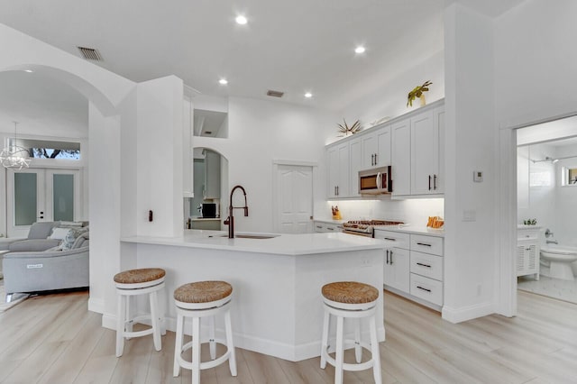 kitchen with a sink, arched walkways, appliances with stainless steel finishes, a breakfast bar area, and light countertops