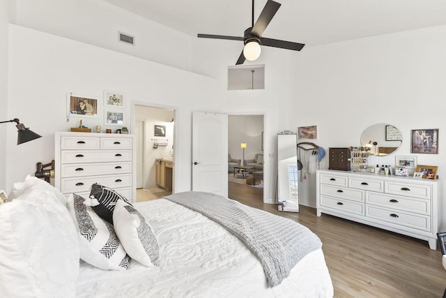 bedroom with visible vents, connected bathroom, ceiling fan, a towering ceiling, and wood finished floors