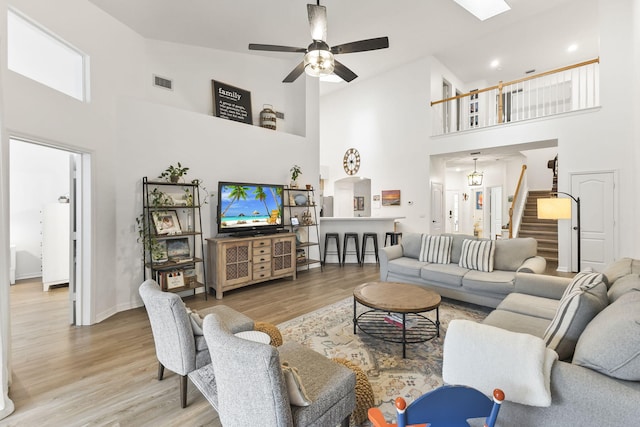 living area with visible vents, a ceiling fan, wood finished floors, a high ceiling, and stairs