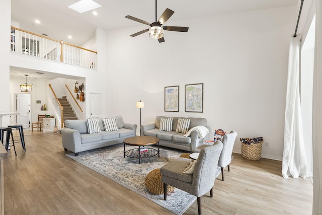 living area with ceiling fan, stairway, a skylight, a high ceiling, and wood finished floors