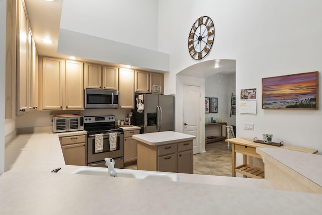 kitchen featuring arched walkways, a sink, light countertops, appliances with stainless steel finishes, and a center island