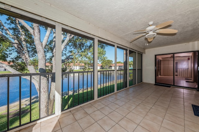 unfurnished sunroom featuring ceiling fan and a water view