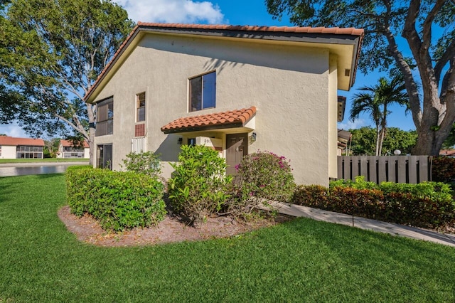 view of property exterior featuring stucco siding, a tile roof, a yard, and fence