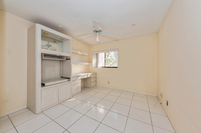 spare room featuring light tile patterned floors, built in desk, baseboards, and ceiling fan