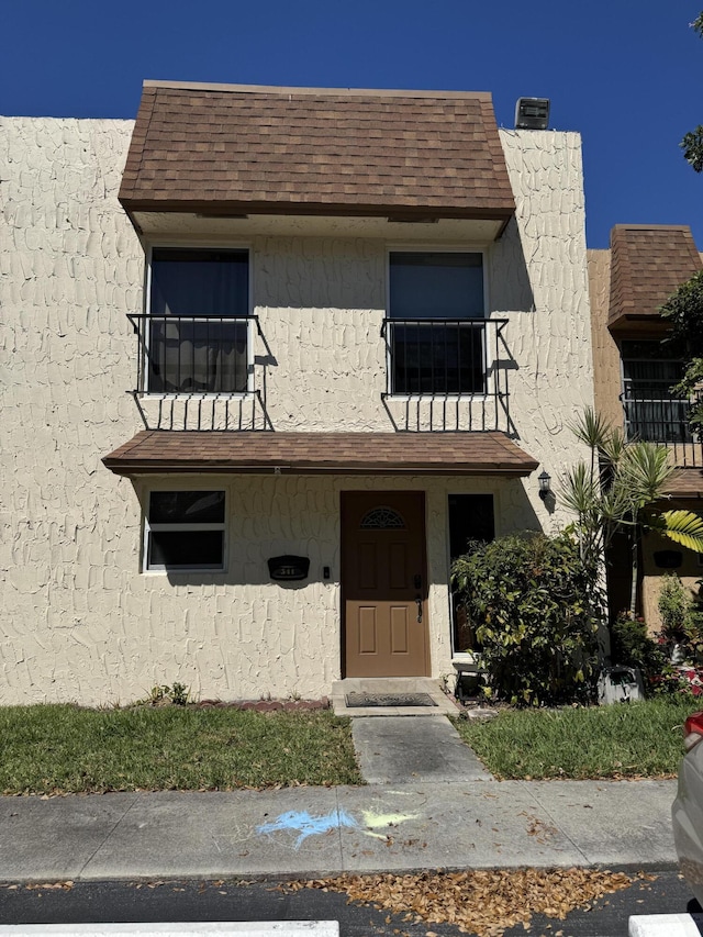 view of front of home with stucco siding, mansard roof, and a shingled roof