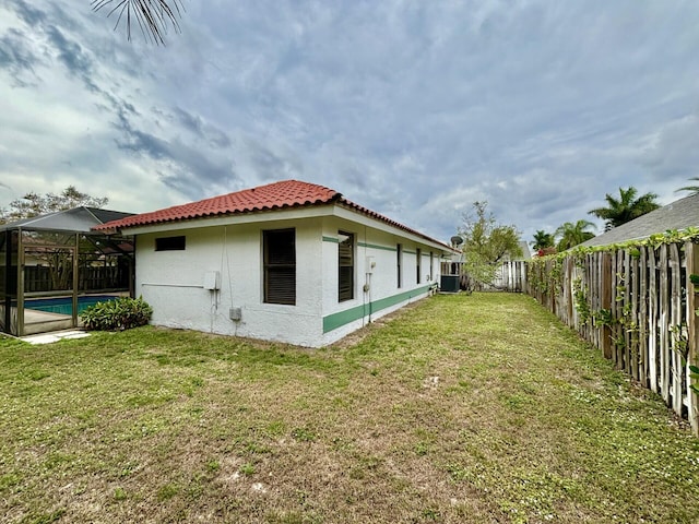 back of house featuring central AC, stucco siding, glass enclosure, a lawn, and a fenced backyard