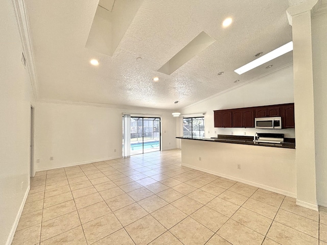 kitchen with dark countertops, vaulted ceiling with skylight, a textured ceiling, stainless steel microwave, and open floor plan