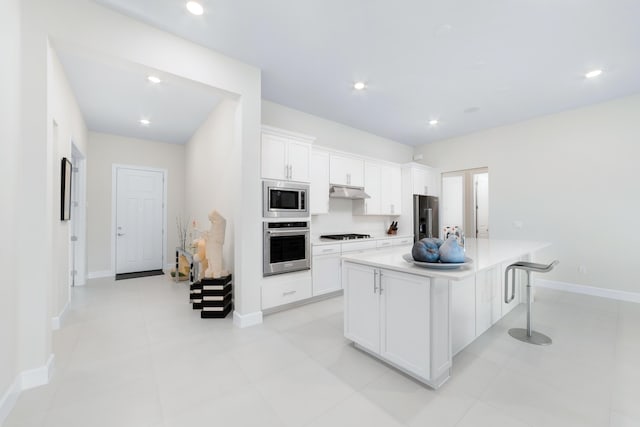 kitchen featuring under cabinet range hood, a kitchen island, white cabinetry, stainless steel appliances, and light countertops