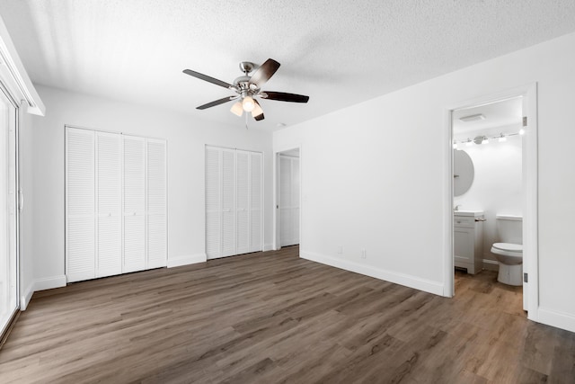 unfurnished bedroom with wood finished floors, baseboards, multiple closets, ensuite bathroom, and a textured ceiling