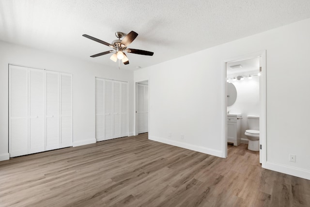 unfurnished bedroom featuring wood finished floors, baseboards, ensuite bath, a textured ceiling, and two closets