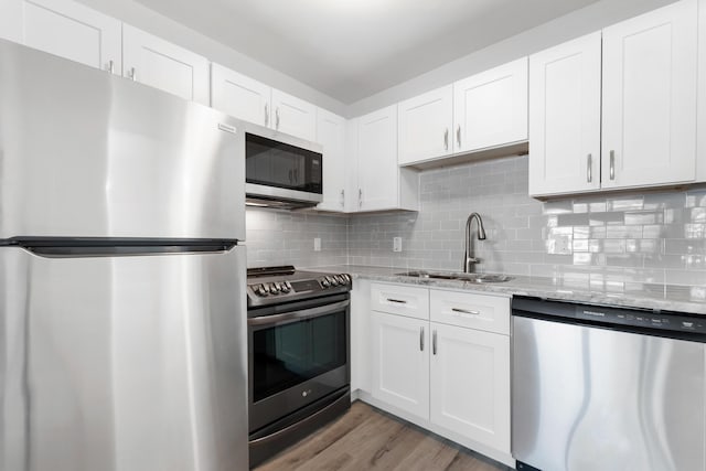 kitchen featuring decorative backsplash, stainless steel appliances, light wood-style floors, white cabinetry, and a sink