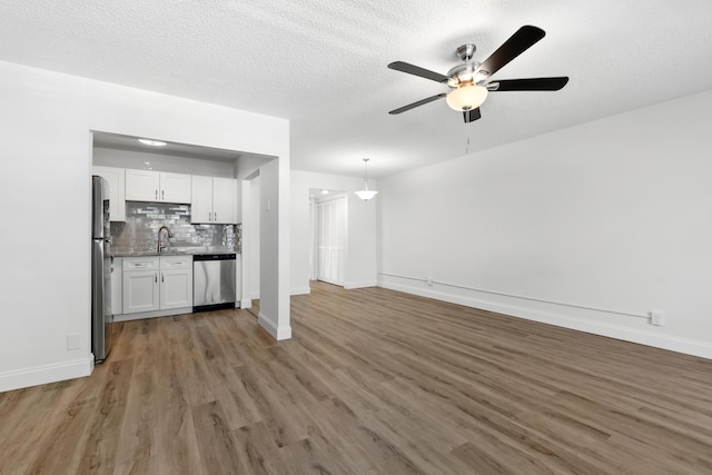 unfurnished living room with a textured ceiling, light wood-type flooring, baseboards, and a sink