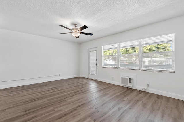 empty room featuring a wall mounted air conditioner, baseboards, and wood finished floors