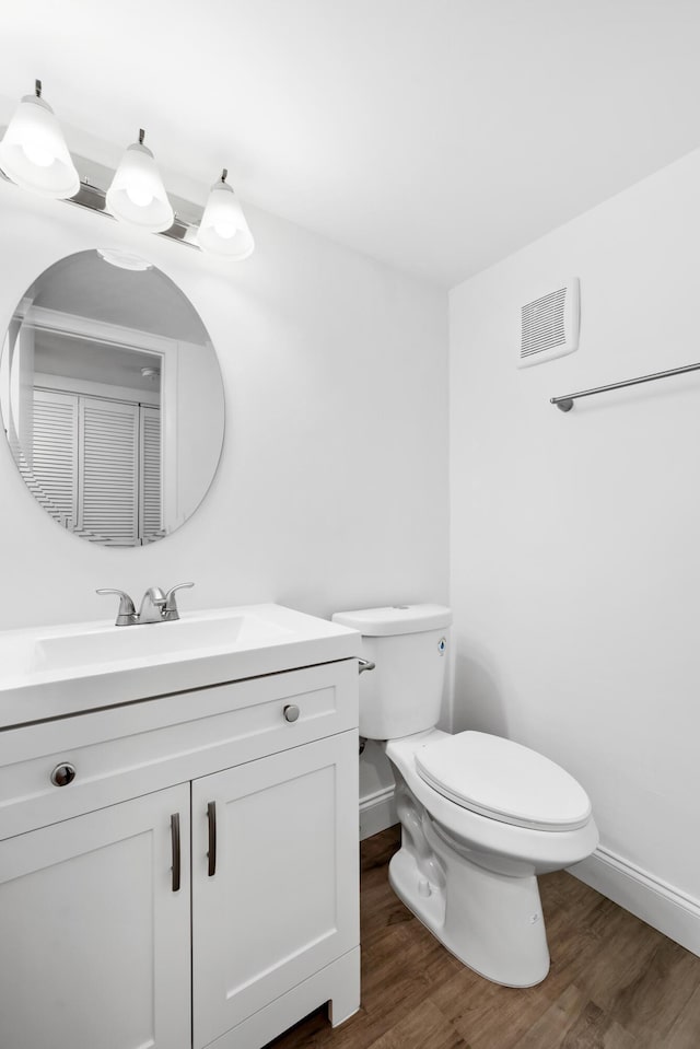 half bathroom with visible vents, toilet, vanity, and wood finished floors