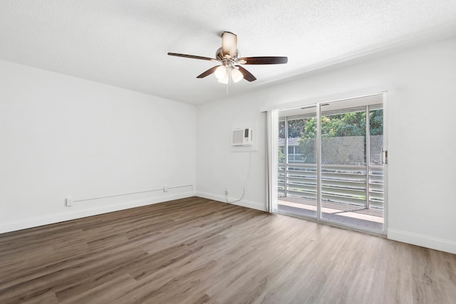 spare room featuring a textured ceiling, wood finished floors, a wall unit AC, baseboards, and ceiling fan