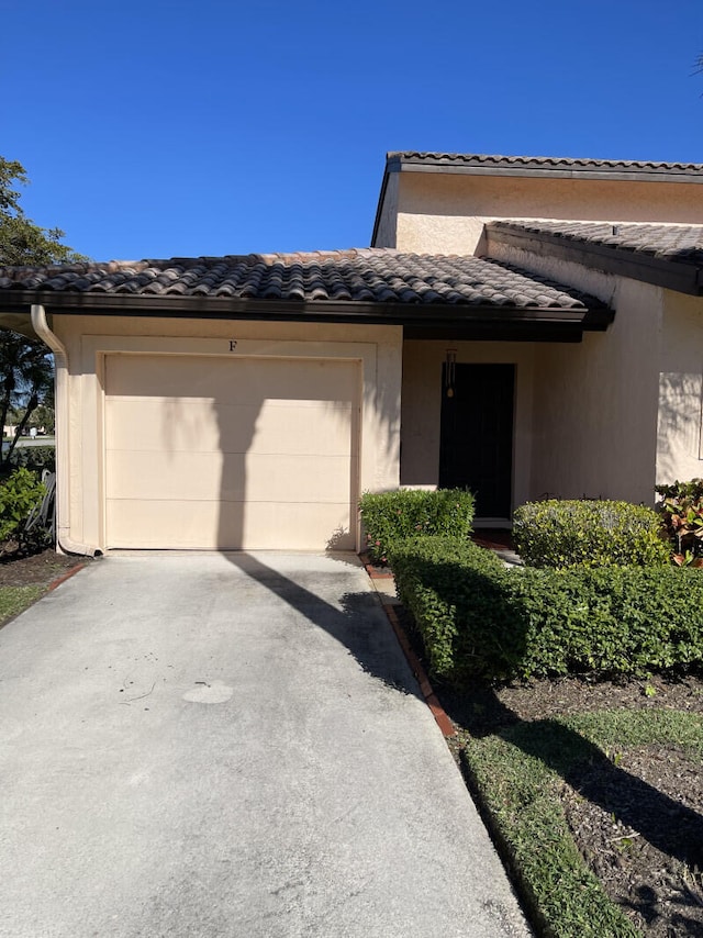 view of front of house with a tiled roof, a garage, driveway, and stucco siding