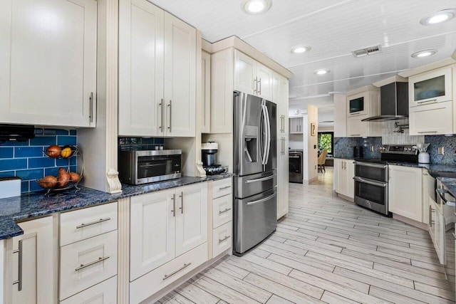 kitchen with visible vents, light wood-style floors, appliances with stainless steel finishes, wall chimney exhaust hood, and decorative backsplash