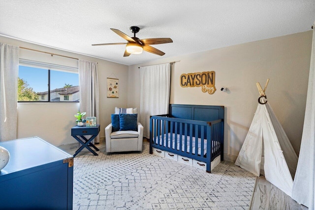 bedroom featuring a nursery area, a ceiling fan, and a textured ceiling