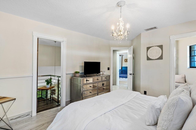 bedroom featuring light wood finished floors, visible vents, a textured ceiling, and a notable chandelier