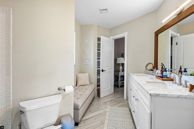 full bath with a sink, visible vents, toilet, and double vanity