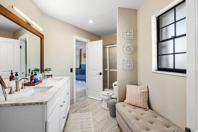 bathroom featuring a shower stall, toilet, double vanity, and a sink