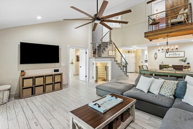 living room with baseboards, stairway, ceiling fan with notable chandelier, wood finished floors, and high vaulted ceiling