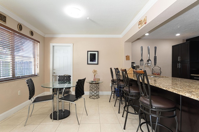 dining room featuring light tile patterned floors, baseboards, a bar, and crown molding