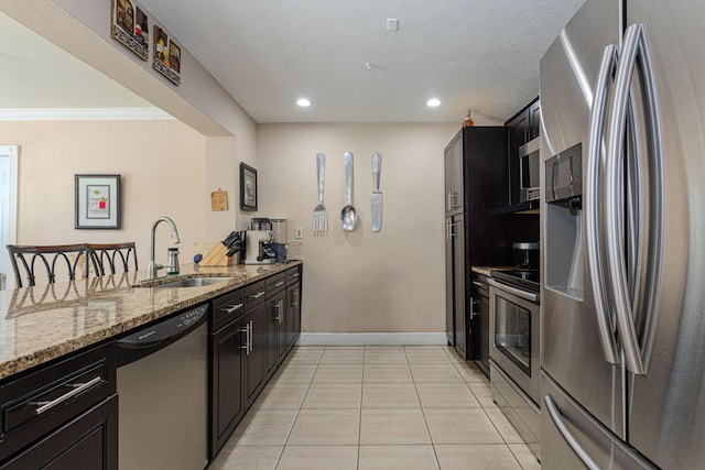 kitchen with light stone countertops, a peninsula, light tile patterned flooring, a sink, and stainless steel appliances