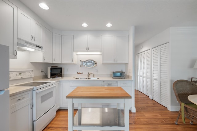 kitchen with under cabinet range hood, light countertops, white cabinets, white appliances, and a sink