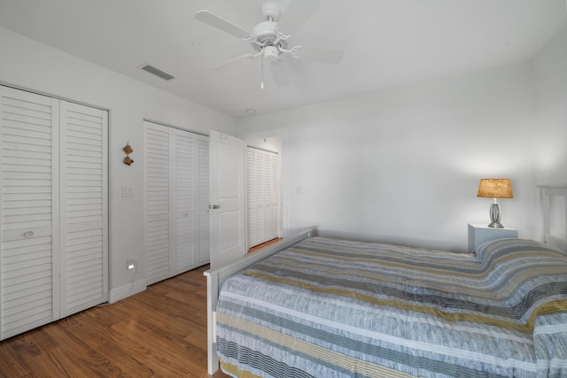 bedroom featuring visible vents, baseboards, multiple closets, wood finished floors, and a ceiling fan