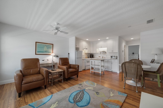 living room with visible vents, a textured ceiling, recessed lighting, light wood-style floors, and baseboards