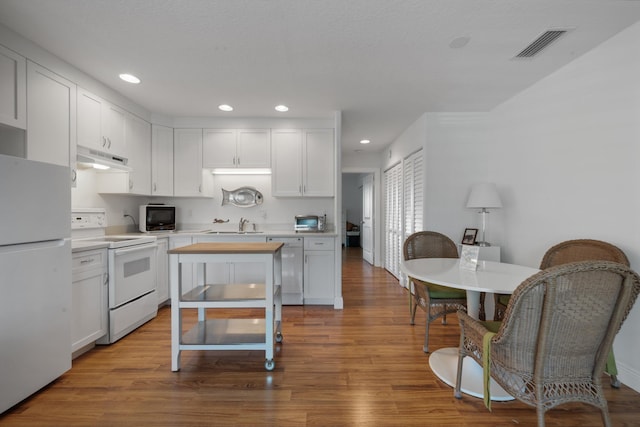 kitchen with visible vents, under cabinet range hood, wood finished floors, white cabinetry, and white appliances