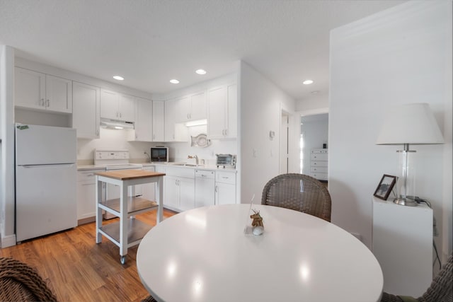 kitchen with white appliances, a sink, light wood-style floors, under cabinet range hood, and white cabinetry