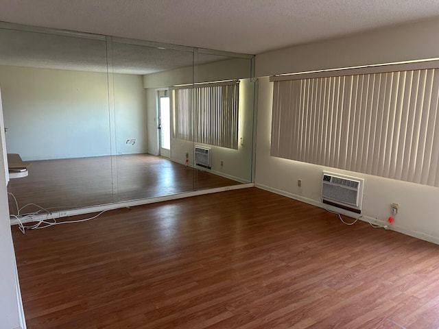 unfurnished room with a textured ceiling, wood finished floors, and a wall mounted AC