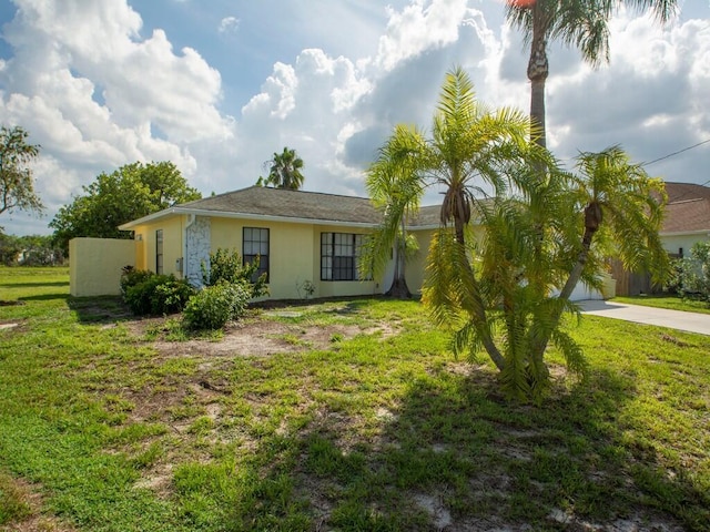 rear view of property with stucco siding, a yard, and driveway